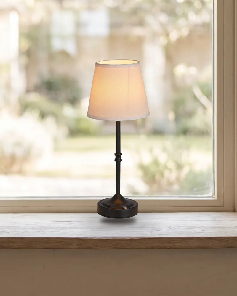 Small cordless table lamp with a fabric shade glowing warm on a windowsill
