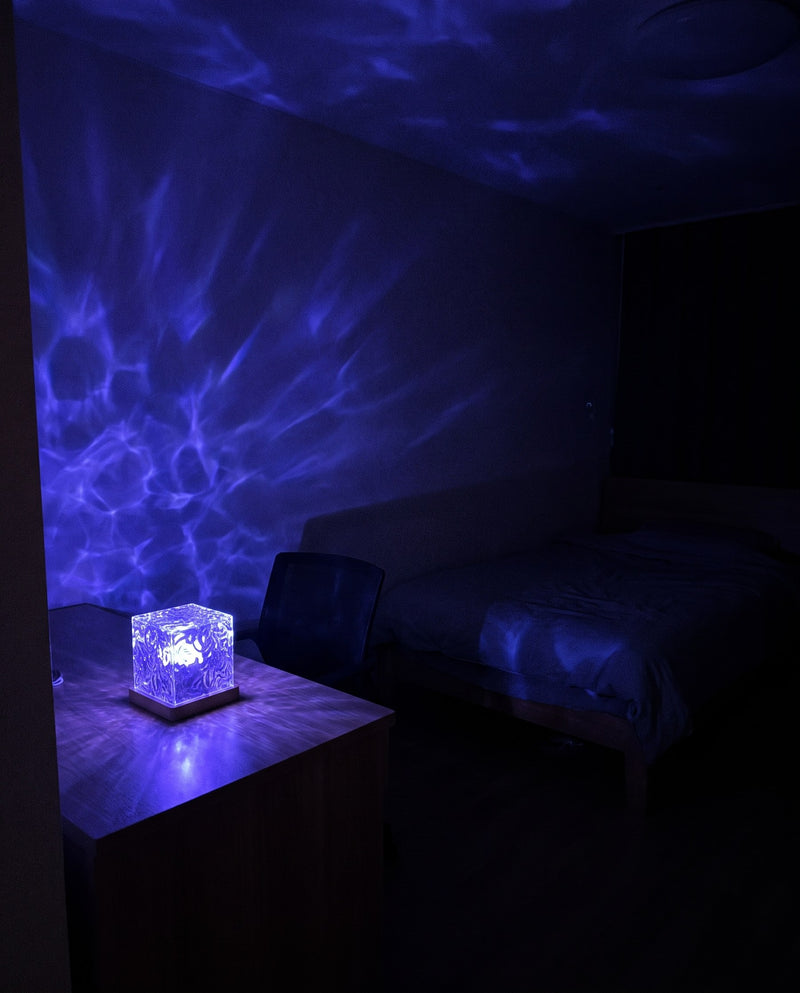 Water ripple lamp on a desk in a dark bedroom, blue ripples across the wall and ceiling